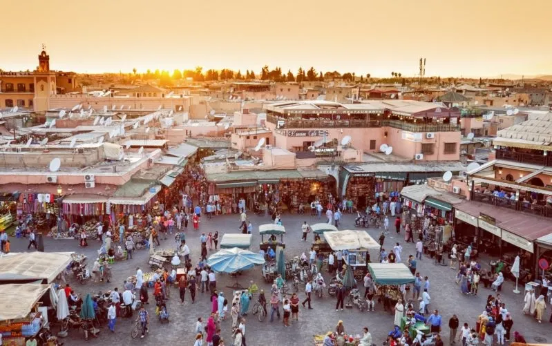 A vibrant sunset casts warm hues over the city of Marrakech, highlighting its unique architecture and bustling atmosphere.