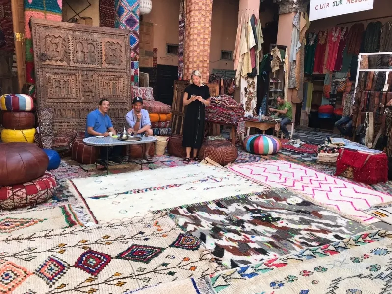 A man and woman sit on a rug, surrounded by Moroccan architecture, in a cozy and inviting indoor setting.