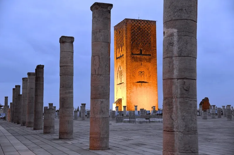 Tall Moroccan columns illuminated at dusk, showcasing intricate architectural details against a twilight sky.