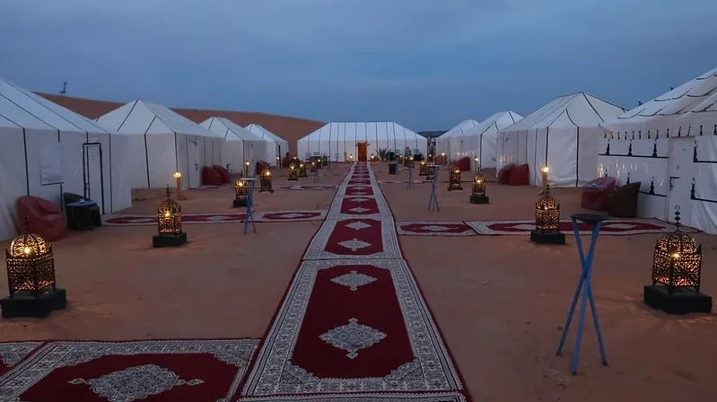 A luxurious Moroccan desert camp featuring tents and a carpeted walkway amidst the sandy landscape.