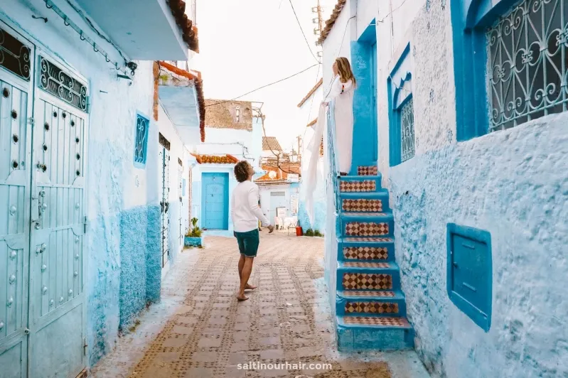 A man strolls through a narrow alley in Chefchaouen, known for its striking blue buildings and vibrant atmosphere.