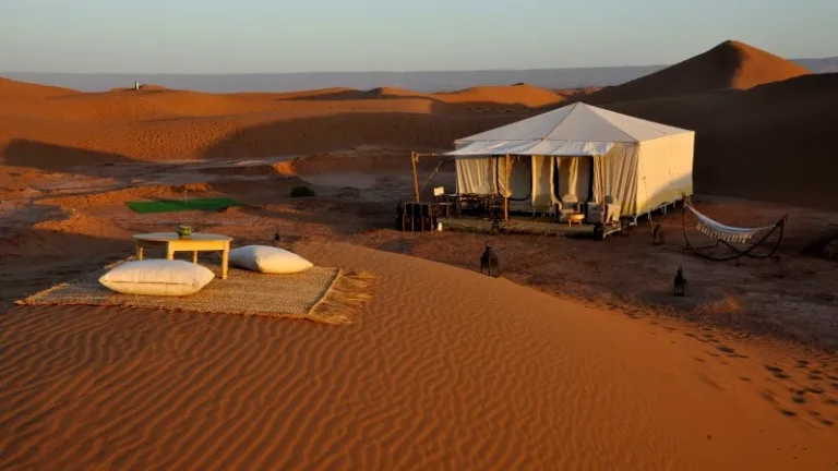 A luxurious tent in the Sahara Desert, featuring a table and chairs, set for an elegant dining experience.