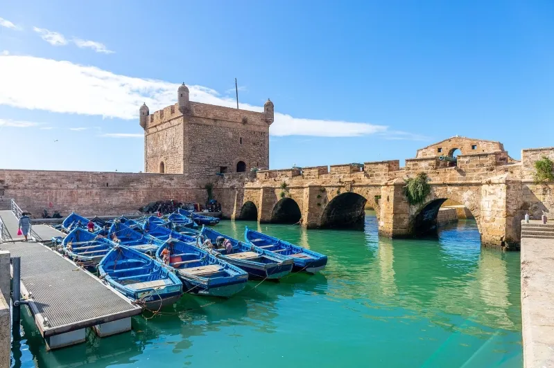 Boats docked in tranquil waters beside a historic castle, showcasing morocco budget travel.