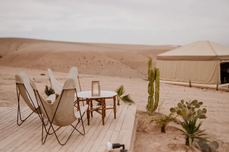 Elegant tent set in the Moroccan desert, surrounded by chairs and a cactus, epitomizing with morocco luxury camps.