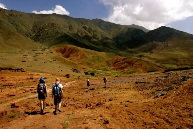 Three individuals trek along a dirt path in the mountains of Morocco, surrounded by stunning natural scenery.