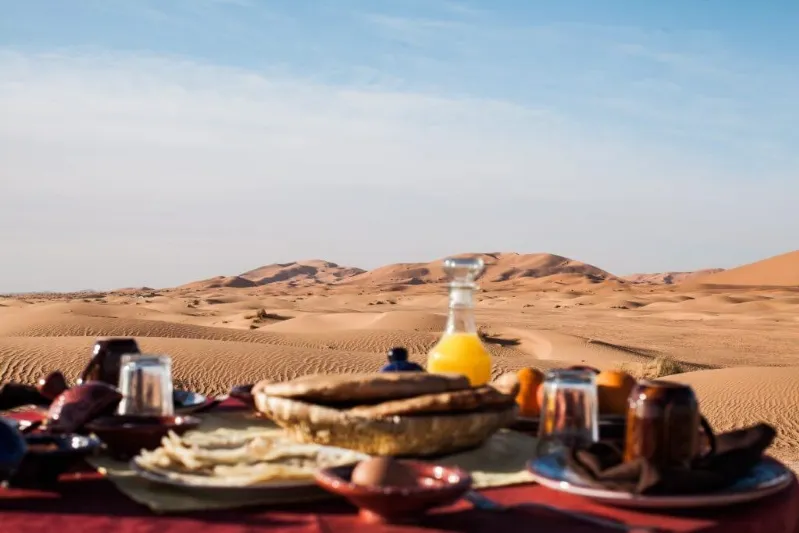 A serene breakfast setting in the desert, showcasing traditional Moroccan dishes against a stunning arid landscape.