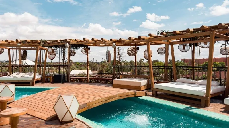 A luxurious wooden deck featuring a pool and lounge chairs, set against the backdrop of a morocco desert luxury camp. 