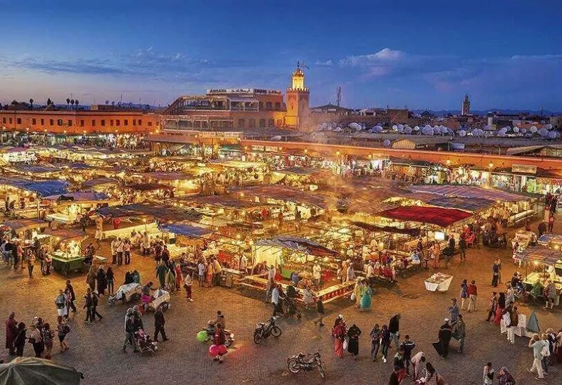 The Marrakech market at dusk, filled with lively vendors and shoppers, capturing the essence of Moroccan culture and Fes desert tours.