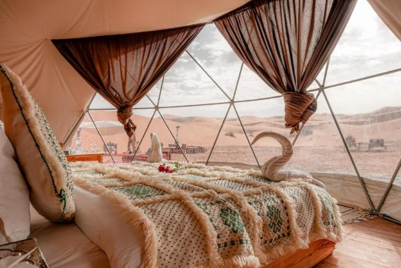 A luxurious tented bed overlooking the vast expanse of the morocco desert luxury camp, showcasing comfort in a serene landscape.