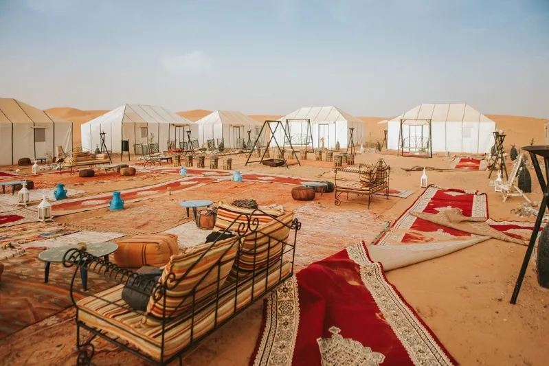 A vibrant Moroccan desert scene featuring tents and furniture, showcasing the unique culture and lifestyle of the region.