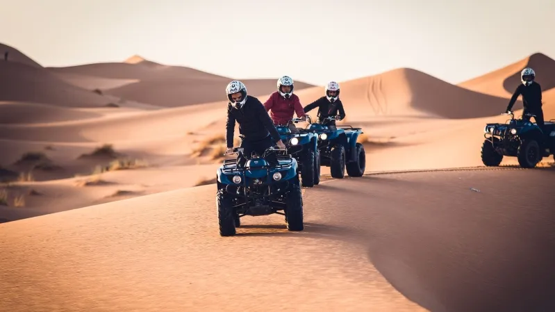 Four riders on quad bikes traverse the Moroccan Sahara Desert, highlighting the adventure in the arid landscape.