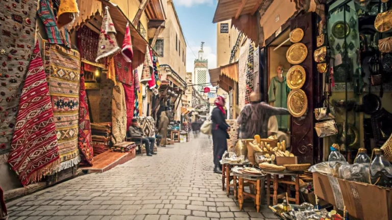 A bustling narrow street in Morocco, filled with people walking and engaging in daily life activities.