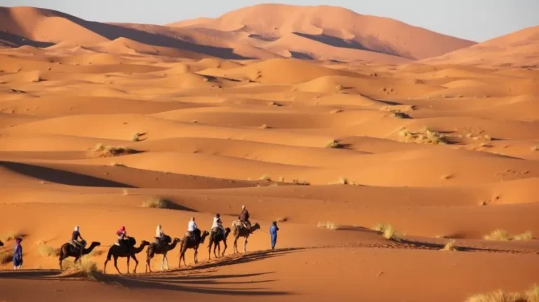 Tourists riding camels across the vast Moroccan desert during a private tour, showcasing the stunning landscape.