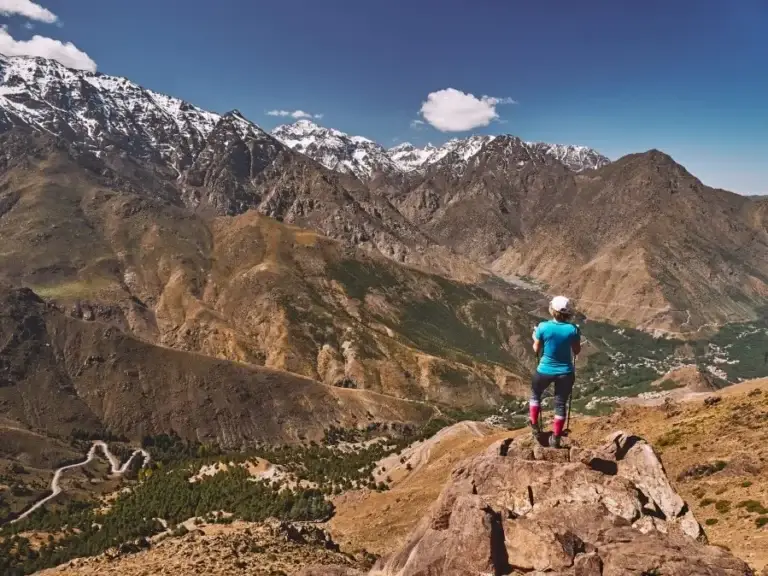 A man stands atop a mountain, gazing over the valley, showcasing the beauty of Atlas Mountains trekking tours.