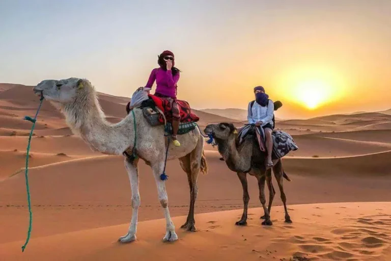 Two individuals riding camels through a desert landscape at sunset, showcasing the beauty of Best Tours in Morocco.