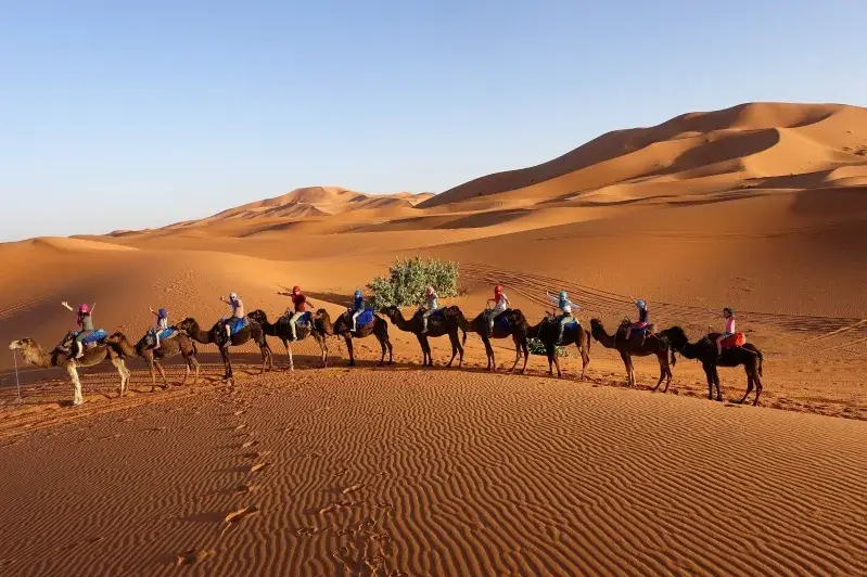 A family enjoying a camel ride in the desert during their Family Morocco Tours, surrounded by vast sandy landscapes.