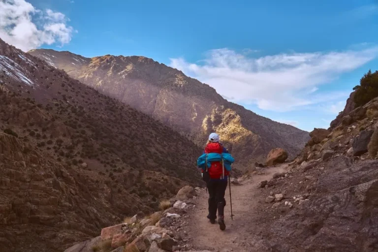 A man with a backpack ascends a mountain trail in Morocco, surrounded by stunning natural scenery.