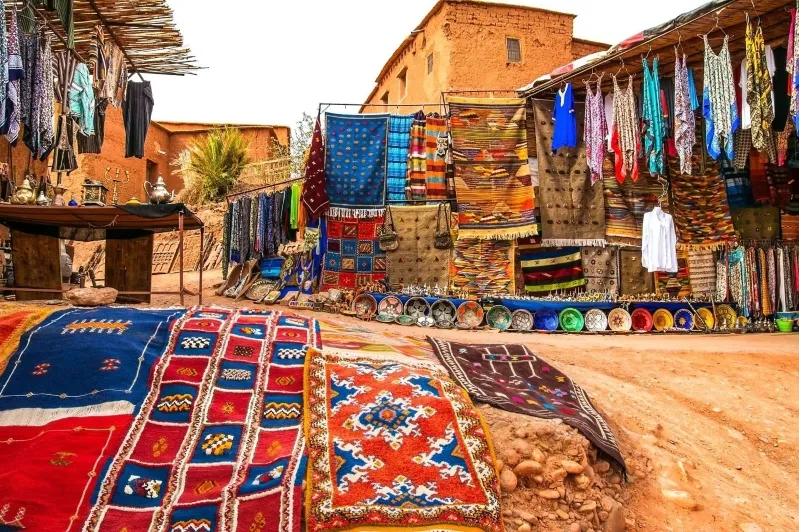 A vibrant market showcasing an array of colorful rugs and clothing, perfect for day trips from Ouarzazate.