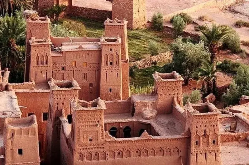An old building surrounded by numerous trees in the desert, showcasing the unique landscape of Ouarzazate.