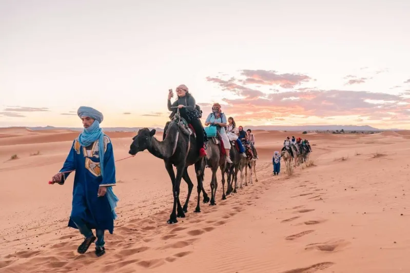 Tourists dressed in blue and turbans riding camels in a desert, highlighting an adventure with top Morocco tour companies. 
