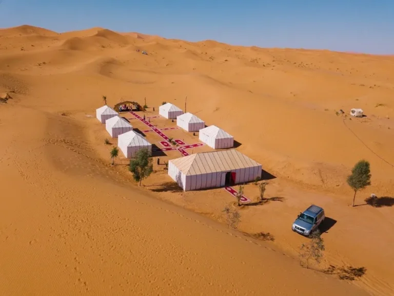 A desert camp in Morocco featuring tents and a car, set against the vast landscape of the Ouarzazate region.