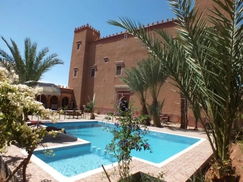 A large pool in front of a grand hotel building in Ouarzazate, Morocco, reflecting the clear blue sky.