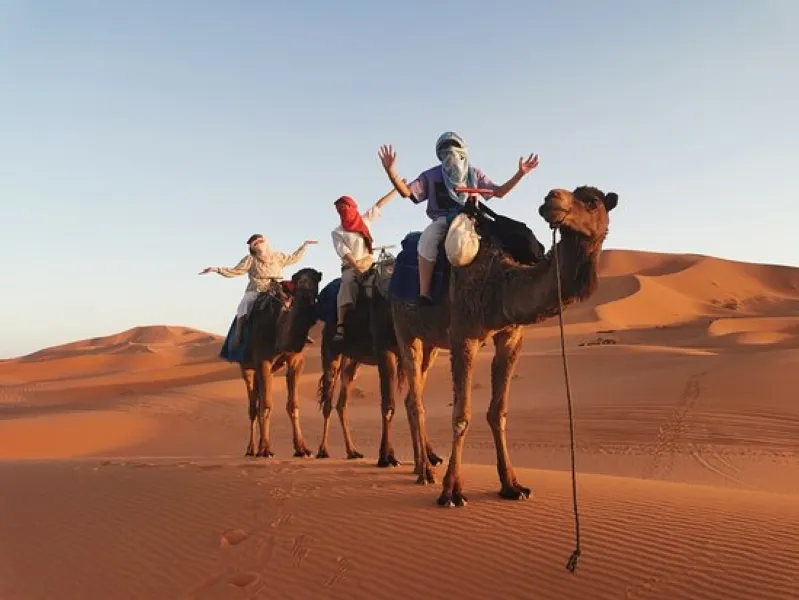 Three individuals riding camels across the vast expanse of the Morocco desert tour Ouarzazate.