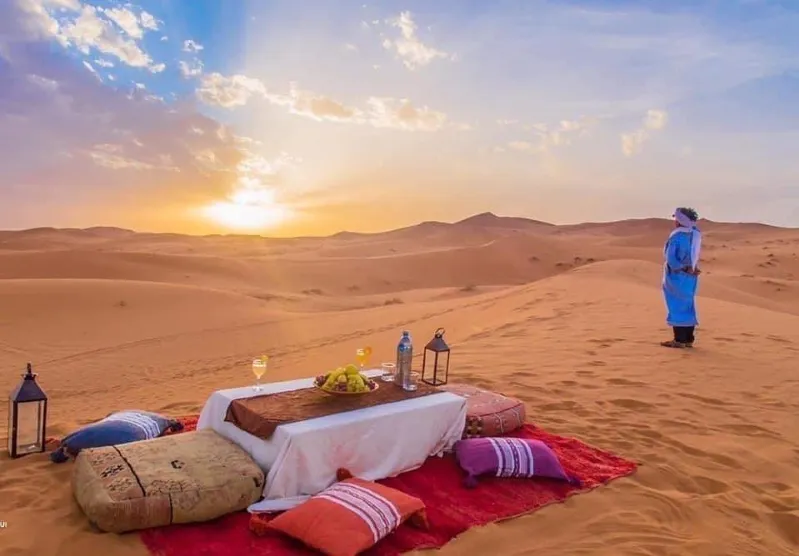 A serene dinner scene in the Sahara Desert at sunset, highlighting the allure of Morocco's best tour experiences.