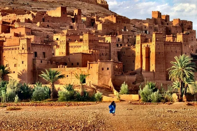 A traveler walks past a desert village in Morocco, showcasing the unique landscape and architecture of the region.