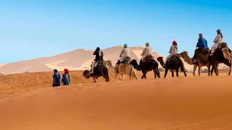 A small group of people riding camels across the sandy desert landscape in Morocco during a tour.