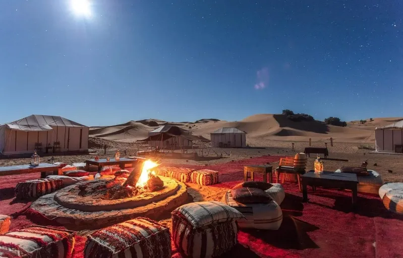 A fire pit surrounded by desert landscape under a bright full moon, ideal for small group tours in Morocco. 