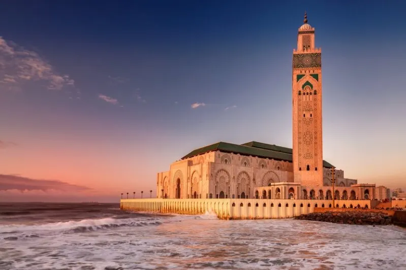  The Hassan II Mosque in Casablanca silhouetted against a vibrant sunset, showcasing Morocco's architectural beauty.
