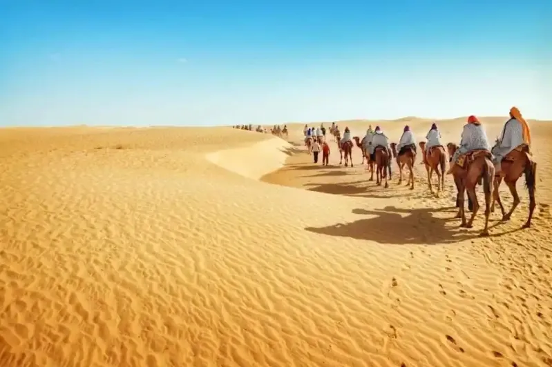 Tourists enjoying a camel ride in the desert, highlighting an adventurous trip to Morocco from the USA.