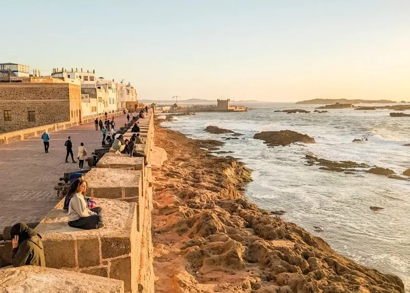 Visitors relax on a wall, overlooking the ocean, highlighting the experience of all-inclusive vacations in Morocco.