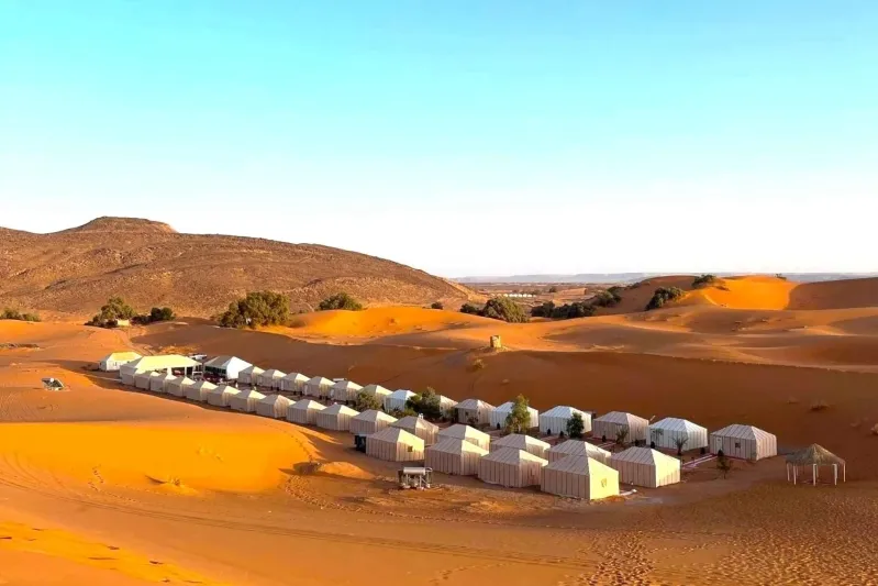 A group of tents set against sand dunes in the desert, showcasing the essence of Morocco Tours Packages.