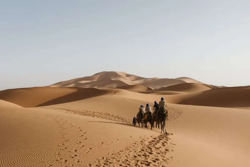  Three riders on camels walk through the desert, representing a travel experience in Casablanca, Morocco.