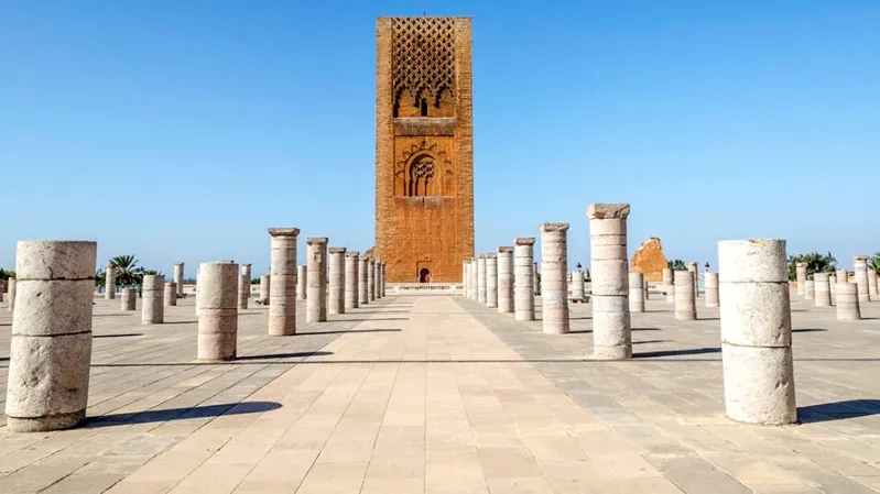 Clock tower of a mosque stands prominently in a plaza, showcasing Moroccan architecture for a travel tour operator. 