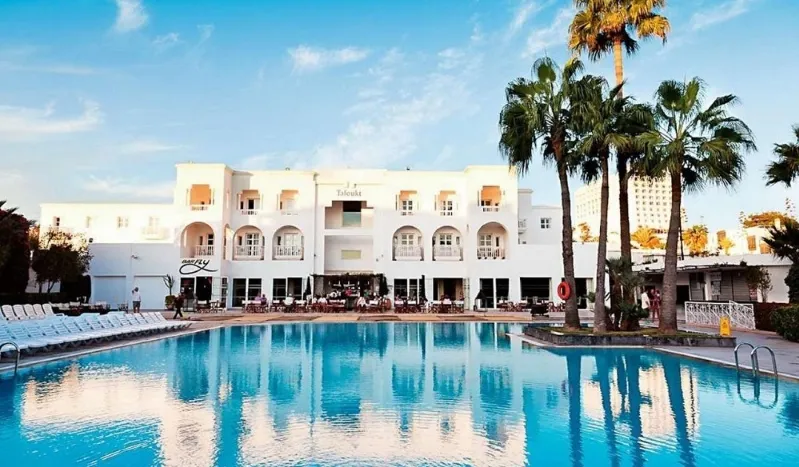 A large hotel pool surrounded by palm trees and lounge chairs, inviting relaxation for a Vacation in Morocco All Inclusive.