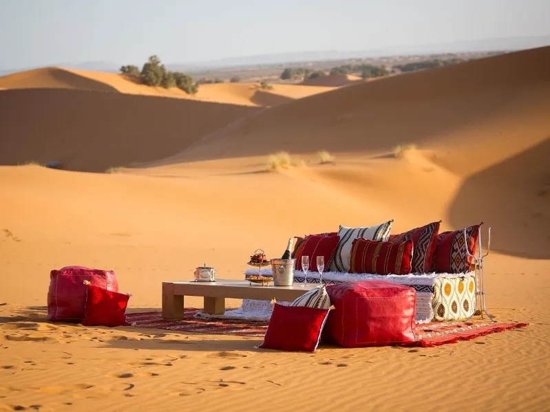 A table and chairs with red cushions set in a desert landscape, ideal for small group luxury tours morocco.