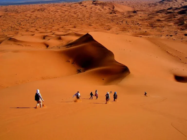 A small group of people walking up a sand dune in the Sahara Desert, showcasing a tour experience in Morocco.