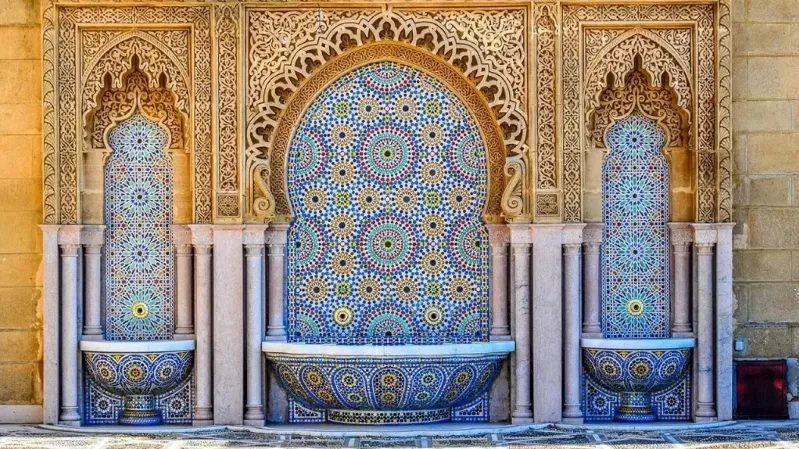 Ornate tiled fountain beside a wall with a door, showcasing Amazigh architecture in Morocco. 