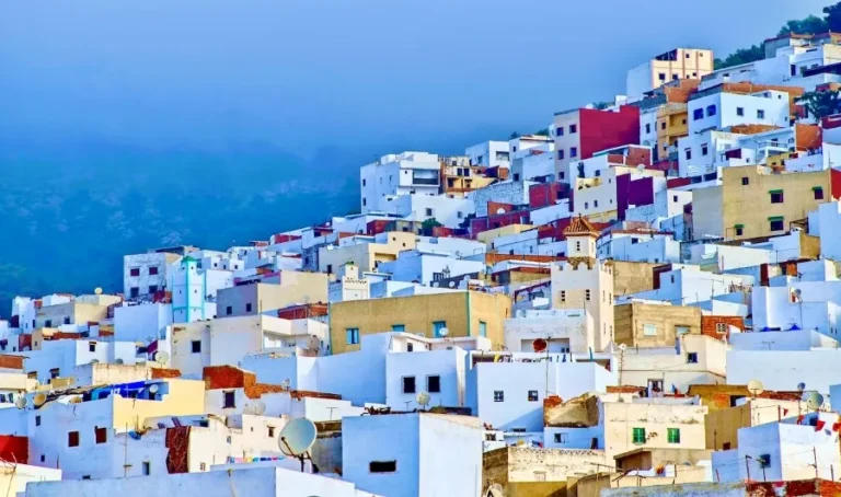 A hillside dotted with white buildings, set against a backdrop of a majestic mountain in Tangier.