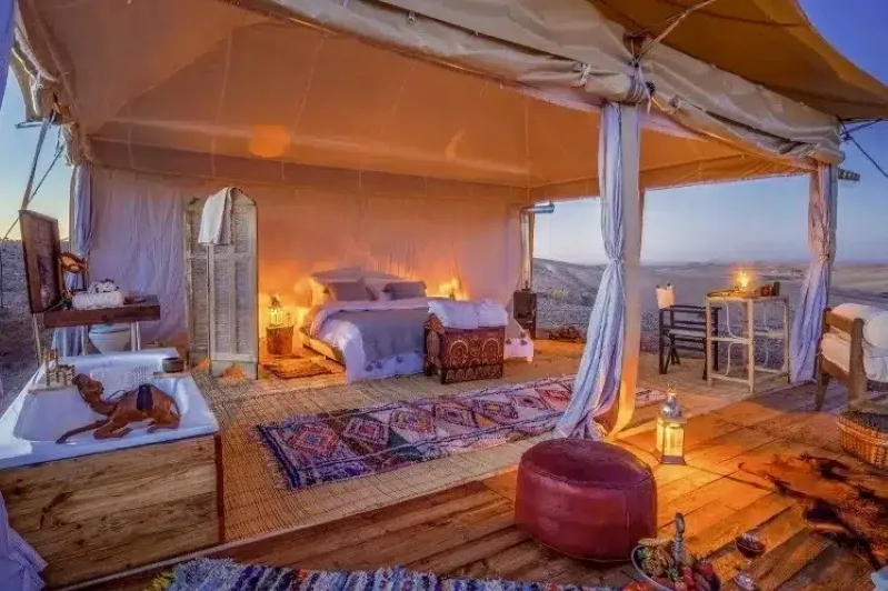 A cozy tent featuring a bed and a bathtub, highlighting luxury camping by the best Morocco private tour company.