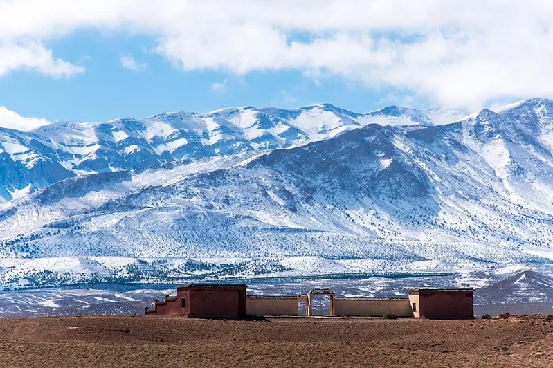 A building in a desert with snow-capped mountains in the background, featured in the Morocco Travel Guide.